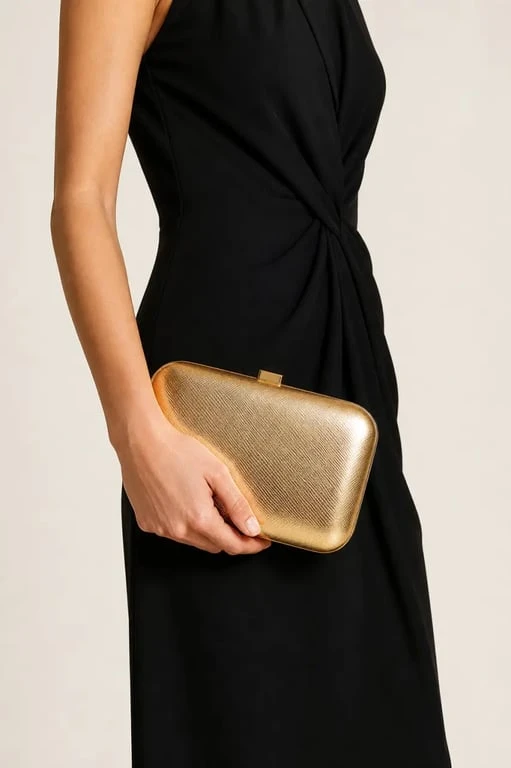 Pochette or élégante portée avec une robe noire de soirée